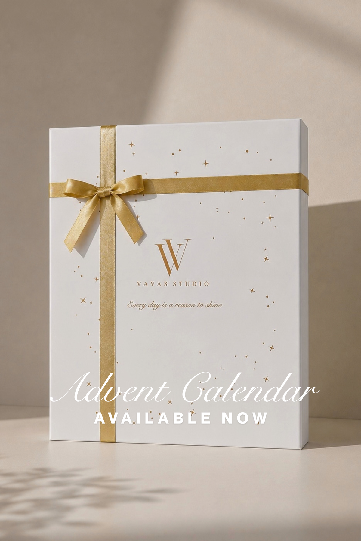 A white gift box for an Advent Calendar from Vavas Studio, tied with a gold ribbon and bow, with gold star confetti details and the text 'Advent Calendar AVAILABLE NOW' on a beige background.