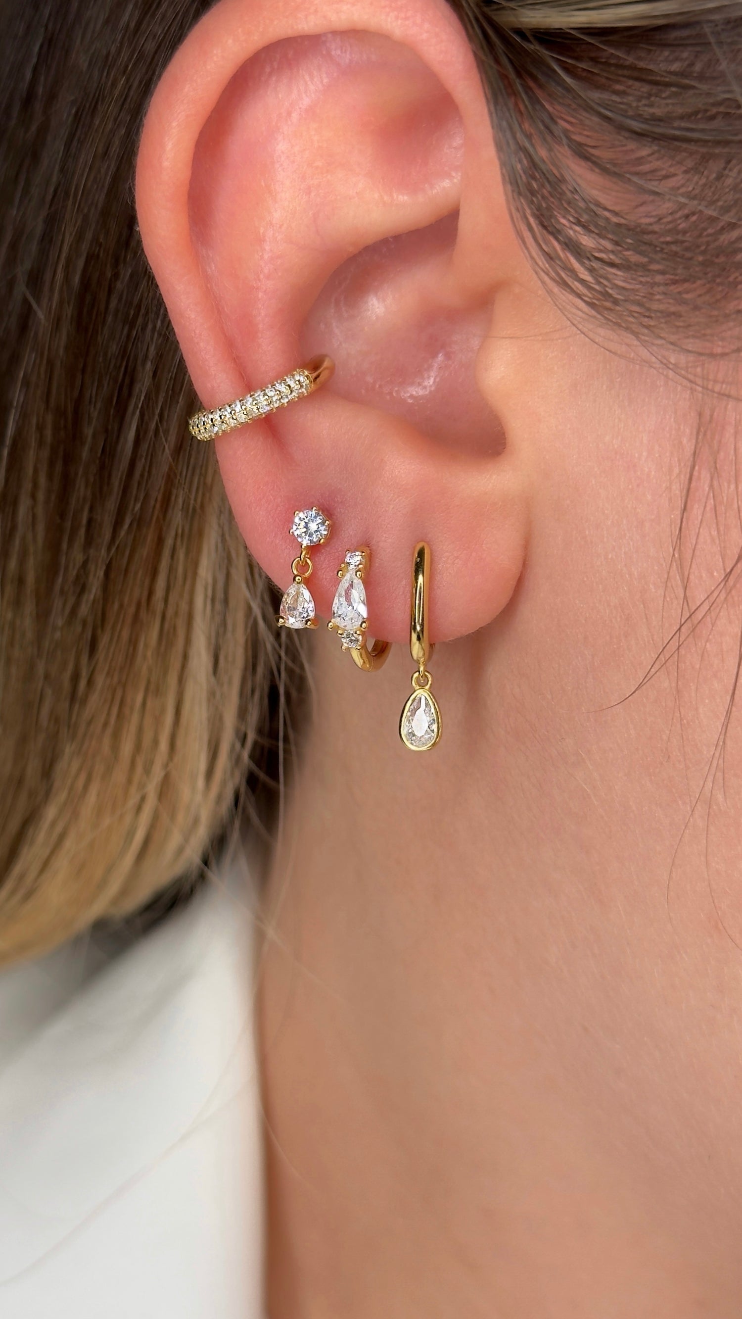 Close-up of an ear with gold hoop earrings and a ring, with a blurred background.