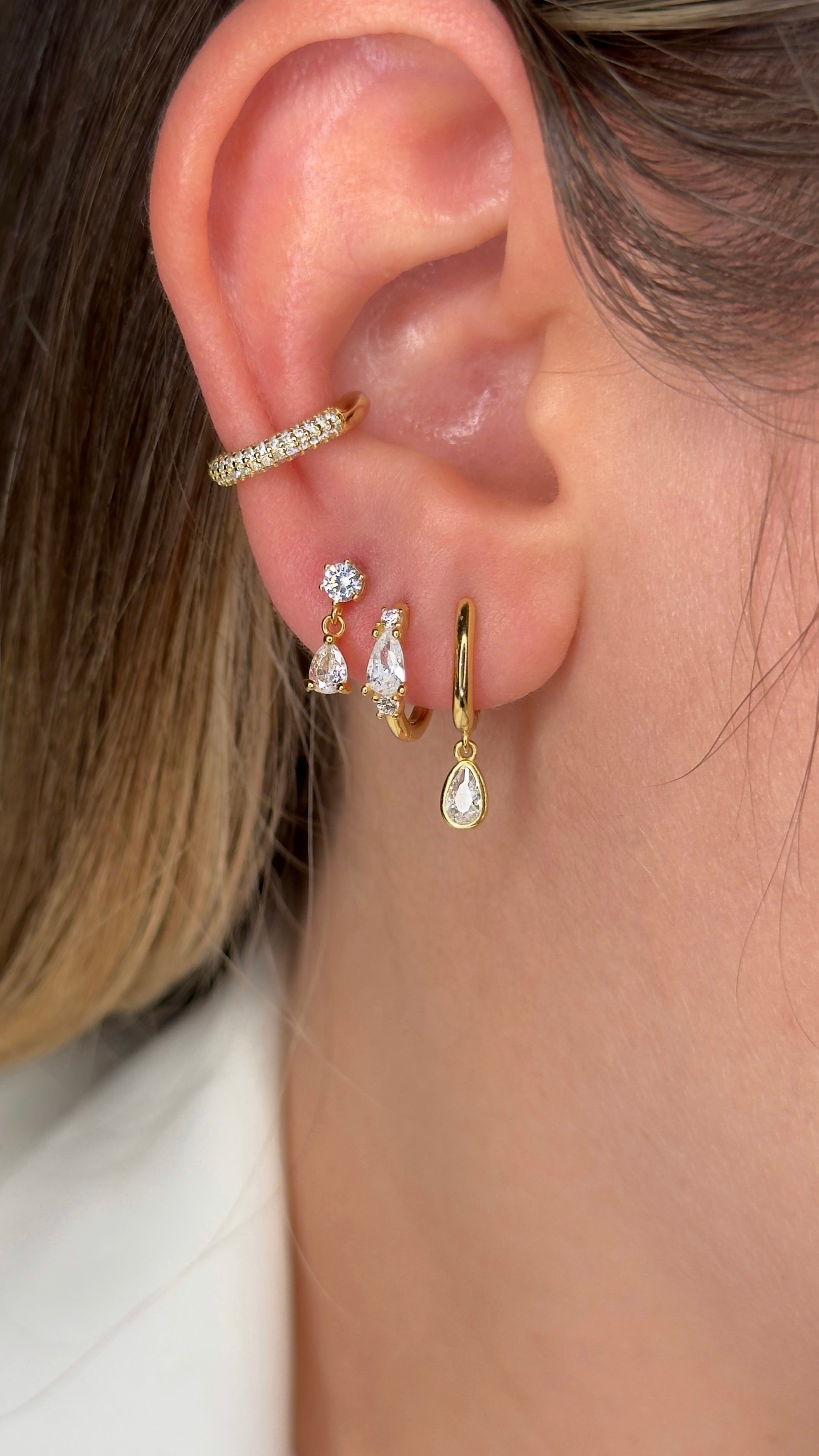 Close-up of an ear with gold hoop earrings and a ring, with a blurred background.